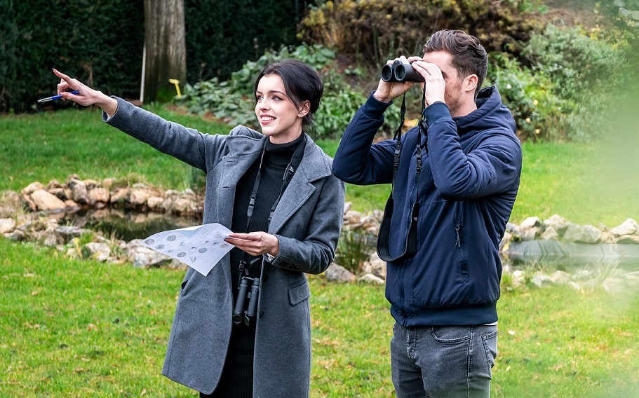 Zwei Menschen treffen sich zur Vogelbeobachtung. Der Mann schaut durch ein Fernglas, während die Frau auf etwas zeigt.